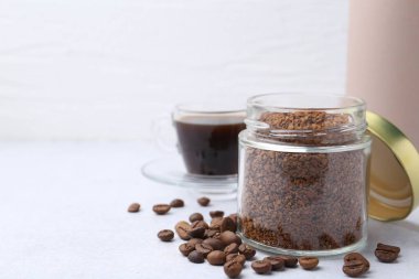 Cam kavanozdaki anlık kahve, fasulye ve sıcak içecek açık gri masada, yakın plan. Metin için boşluk