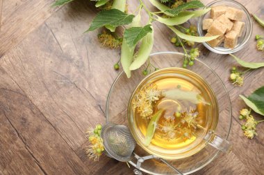 Fincanda taze ıhlamur çayı, şeker küpleri ve tahta masada çiçekler, düz uzanma. Metin için boşluk