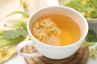 Fincanda taze ıhlamur çayı ve beyaz masada çiçekler, yakın plan.