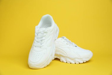 Sarı arka planda bir çift beyaz spor ayakkabı.