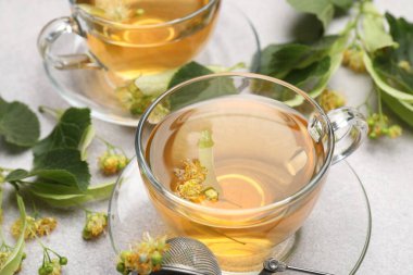 Fincanlarda taze ıhlamur çayı ve açık gri masada çiçekler, yakın plan.