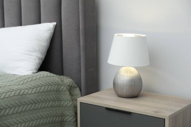 Lamba komodinin üstünde, yatak da beyaz duvarın yanında.