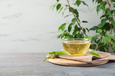 Lezzetli yeşil çay, cam bardakta limon ve gri ahşap masada yapraklar, yazı için yer.