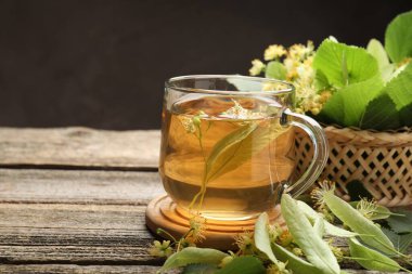 Fincanda lezzetli ıhlamur çayı, ahşap masada yapraklar ve çiçekler koyu arka planda, yakın plan. Metin için boşluk