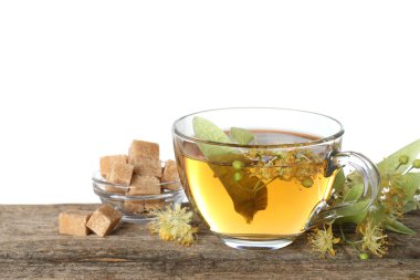 Fincanda nefis ıhlamur çayı, küp şekerler, yapraklar ve çiçekler beyaz arka planda ahşap masada.