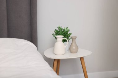 Güzel vazolar ve ev bitkisi yatağın yanındaki beyaz masada.
