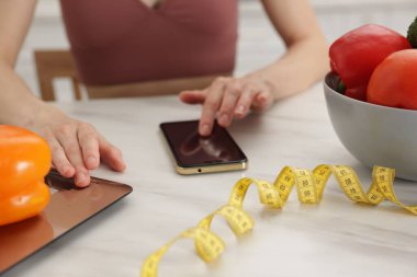 Beyaz mermer masada biber tartırken akıllı telefon kullanan bir kadın. Kapalı alanda.