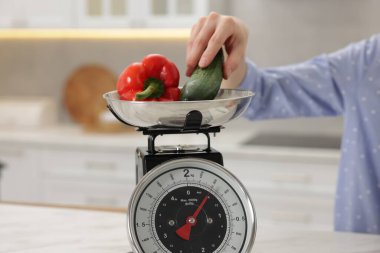 Mutfak terazisinde sebze tartan bir kadın. Beyaz masa içinde, yakın plan.