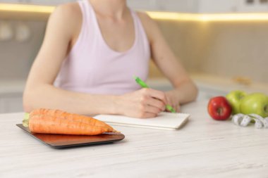 Beyaz ahşap masada beslenme planı geliştiren kadın mutfak ölçeğine ve havuçlara odaklanıyor.