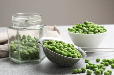 Açık gri masada taze bezelye ve turşu kavanozu, yakın plan.