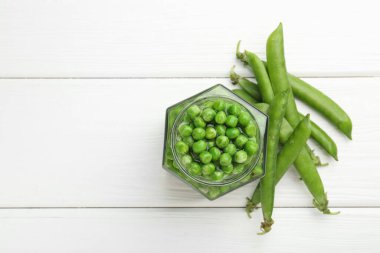 Turşu kavanozundaki taze bezelyeler ve beyaz ahşap masadaki kabuklar düz. Metin için boşluk