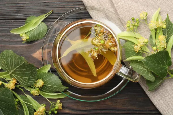 Fincanda taze ıhlamur çayı ve koyu ahşap masada çiçekler.