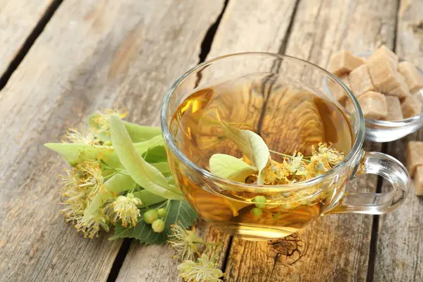 Lezzetli ıhlamur çayı, şeker küpleri, yapraklar ve çiçekler ahşap masada, yakın plan.