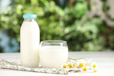 Bardakta taze süt, şişe ve papatya çiçekleri açık havada beyaz ahşap masa üzerinde, mesaj için yer. Süt ürünü