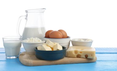 Farklı süt ürünleri ve yumurtalar mavi ahşap masada beyaz arka planda