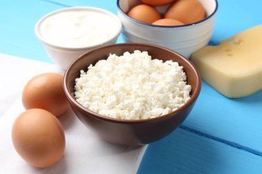 Açık mavi ahşap masa üzerinde farklı süt ürünleri ve yumurtalar.