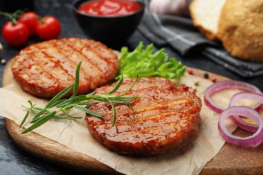 Lezzetli hamburger köfteleri, domatesler ve baharatlar siyah masada, yakın plan.