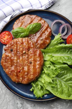 Lezzetli hamburger köfteleri, domates, marul ve baharatlar gri masada, üst tarafta.