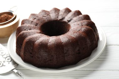 Lezzetli çikolatalı kek, kakao tozu ve beyaz ahşap masada servis, yakın plan.