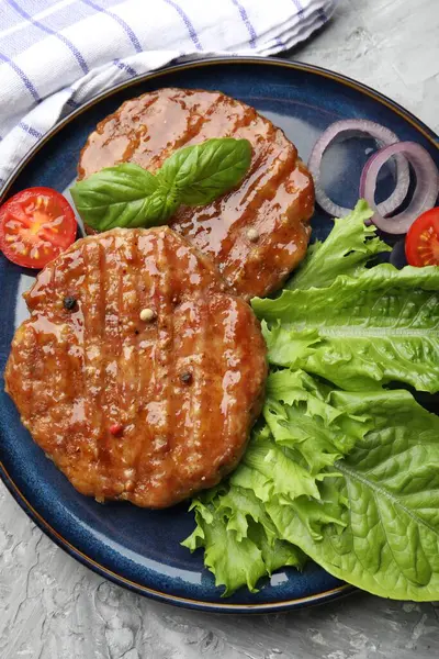 Lezzetli hamburger köfteleri, domates, marul ve baharatlar gri masada, üst tarafta.