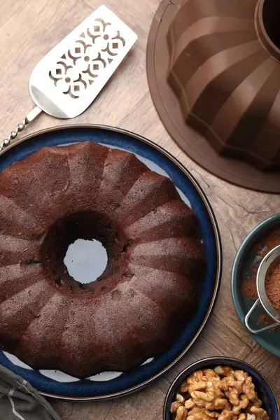 Lezzetli çikolatalı kek, ceviz, kakao tozu ve sunucu ahşap masada, düz uzanmış.