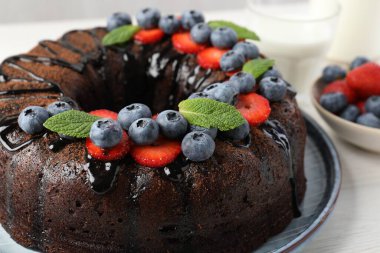 Hafif ahşap masada çilekli, nane ve yaban mersinli lezzetli çikolatalı kek.