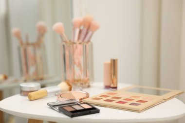 Beyaz masadaki farklı makyaj ürünleri ve fırçalar.