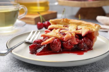 Gri desenli masa üzerinde lezzetli kirazlı turta ve çatal, yakın plan.