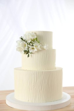 Ahşap masanın üzerinde çiçek dekoru olan nefis düğün pastası beyaz arka planda.