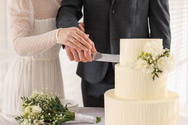 Yeni evliler kapalı bir masada düğün pastasını kesiyorlar.