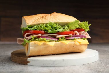 Gri desenli masada jambonlu, peynirli ve sebzeli baget sandviç, bulanık kahverengi arka plan, yakın plan.