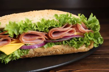 Jambonlu, peynirli ve sebzeli baget sandviç. Ahşap masa, siyah arka plan, yakın plan.