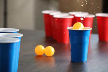 Bira pong oyunu. İçkili plastik bardaklar ve toplar ahşap masada, yakın plan.