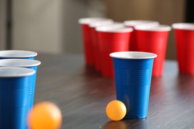Bira pong oyunu. İçkili plastik bardaklar ve toplar ahşap masada, yakın plan.