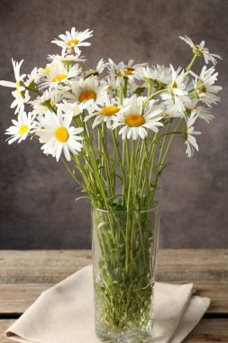 Tahta masadaki vazoda, kahverengi desenli arka planda birçok güzel papatya çiçeği, yakın plan.