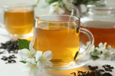 Cam bardakta yasemin çayı, çaydanlık, çiçekler ve kuru yapraklar beyaz masada, yakın plan.