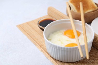 Kavanozda yarı haşlanmış yumurta, soya sosu, yemek çubuğu ve açık gri masada kızarmış ekmek ile geleneksel Asya kahvaltısı, yakın plan. Metin için boşluk
