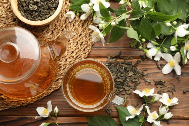 Aromatik yasemin çayı cam fincanda, çaydanlıkta, demlikte ve çiçeklerde ahşap masada, düz yerde.