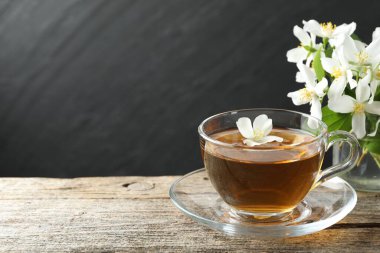 Cam bardakta Aromatik yasemin çayı, tahta masada çiçekler ve yeşil yapraklar, yakın plan. Metin için boşluk