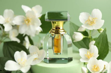 Yeşil arka planda bir şişe parfüm ve yasemin çiçeği, yakın plan.