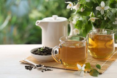 Bardakta yasemin çayı, çaydanlık, beyaz ahşap masada kuru yapraklar ve çiçekler, yakın plan. Metin için boşluk