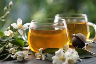 Bardakta lezzetli yasemin çayı, siyah masada kuru yapraklar ve çiçekler, yakın plan.