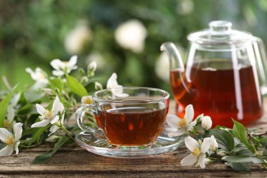 Lezzetli yasemin çayı fincanda, çaydanlık ve çiçekler ahşap masada, yakın plan