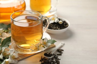 Lezzetli yasemin çayı fincanda, kuru yapraklar ve beyaz ahşap masada çiçekler, yakın plan. Metin için boşluk