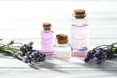 Beyaz ahşap masada doğal yağ ve lavanta çiçekleri, yakın plan.