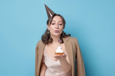 Doğum günü kutlaması. Kekin üzerine mum üfleyen kadın açık mavi arka planda