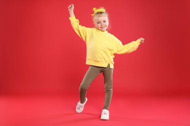 Kırmızı arka planda dans eden tatlı küçük kız.