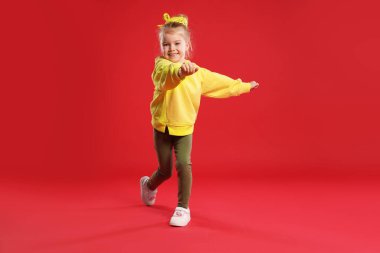 Kırmızı arka planda dans eden tatlı küçük kız.