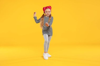 Turuncu arka planda dans eden tatlı küçük kız.