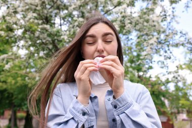 Bahar günü çiçek açan ağacın yanında mevsimlik polen alerjisi olan kağıt mendili olan bir kadın.